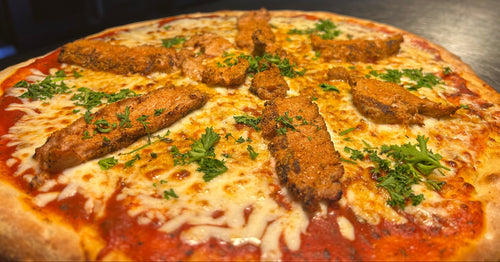 Pizza with fried chicken pieces and cheese on a metal surface