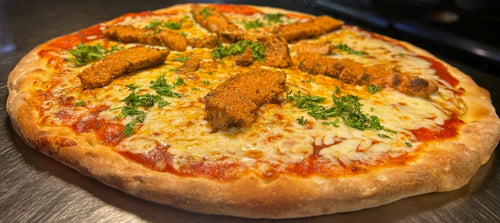 Pizza with chicken pieces and herbs on a metal surface