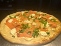 Pizza with salmon and greens on a wooden surface