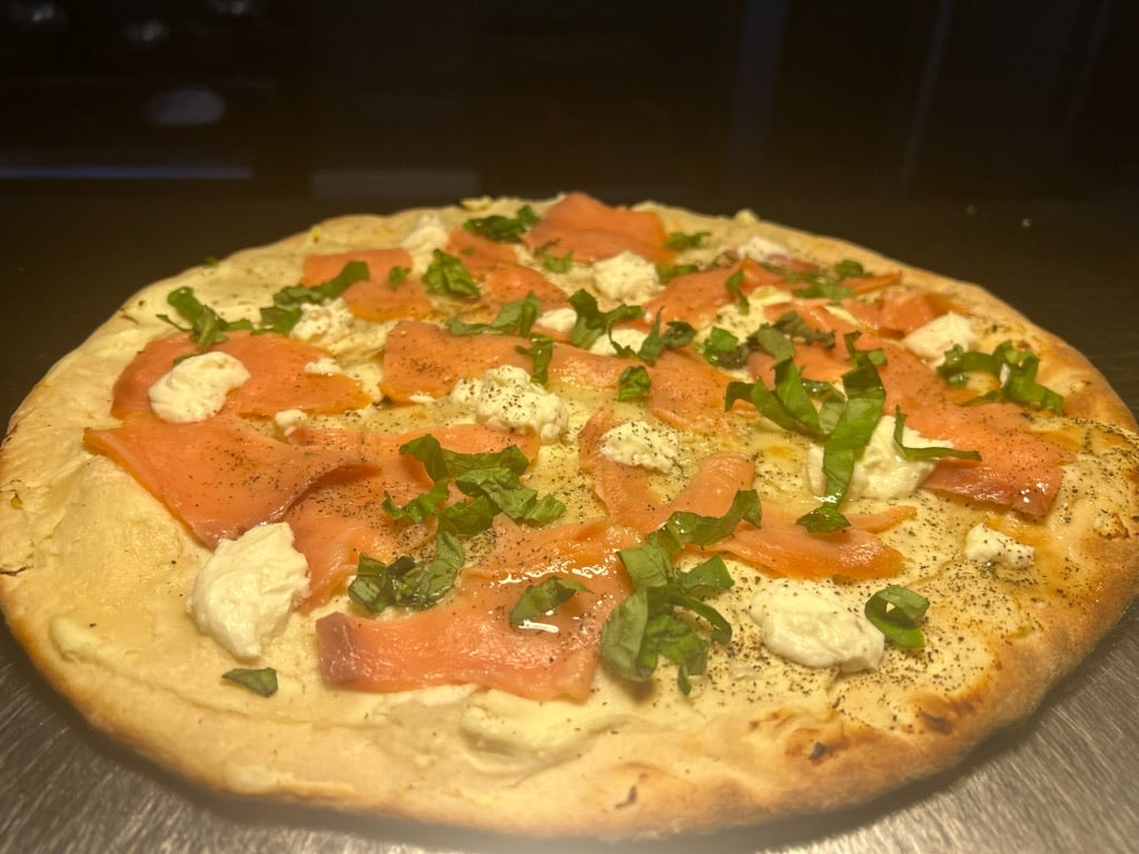 Pizza with salmon and greens on a wooden surface