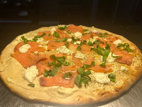 Pizza with salmon and greens on a wooden surface