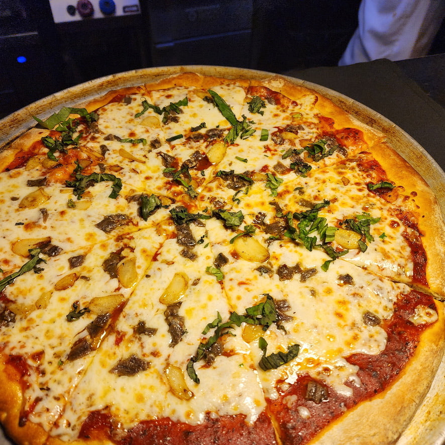 Close-up of a pizza with cheese and spinach toppings on a metal pan.