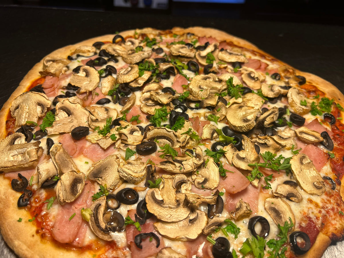 Pizza with mushrooms, olives, and ham on a wooden board