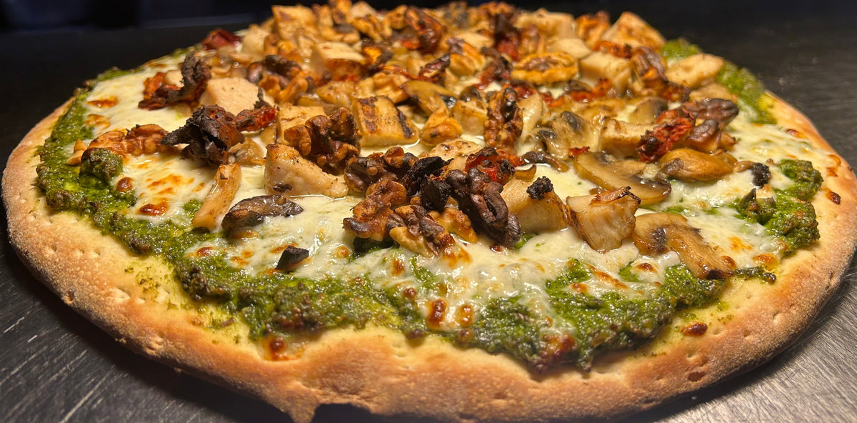 Pizza with pesto and meat toppings on a metal surface