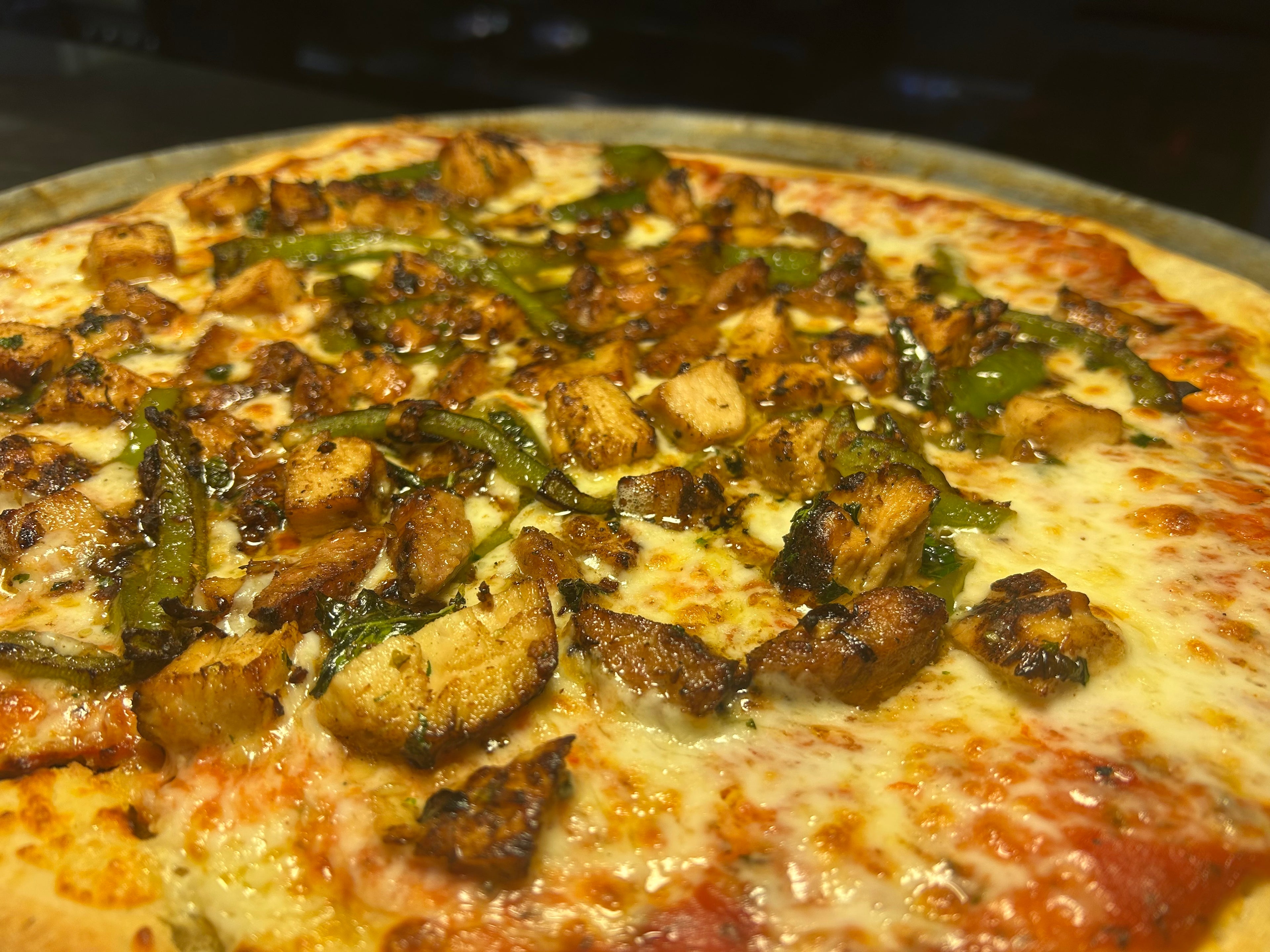 Close-up of a pizza with mushrooms and green peppers on a metal pan.