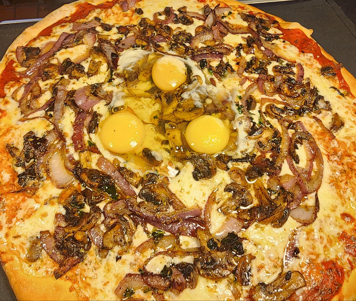 Pizza with multiple egg yolks and various toppings on a wooden table.