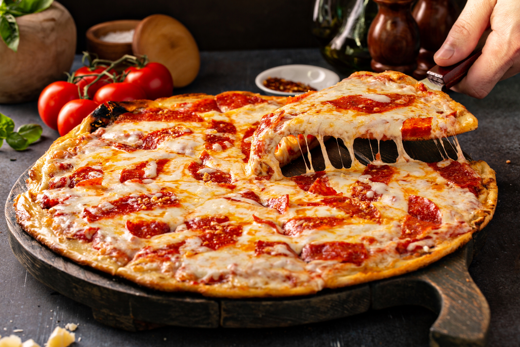 A pizza with tomato sauce, mozzarella, and pepperoni being lifted with a slice by a person's hand.