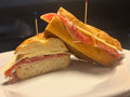 Half-cut sandwich with ham and cheese on a white plate against a dark background