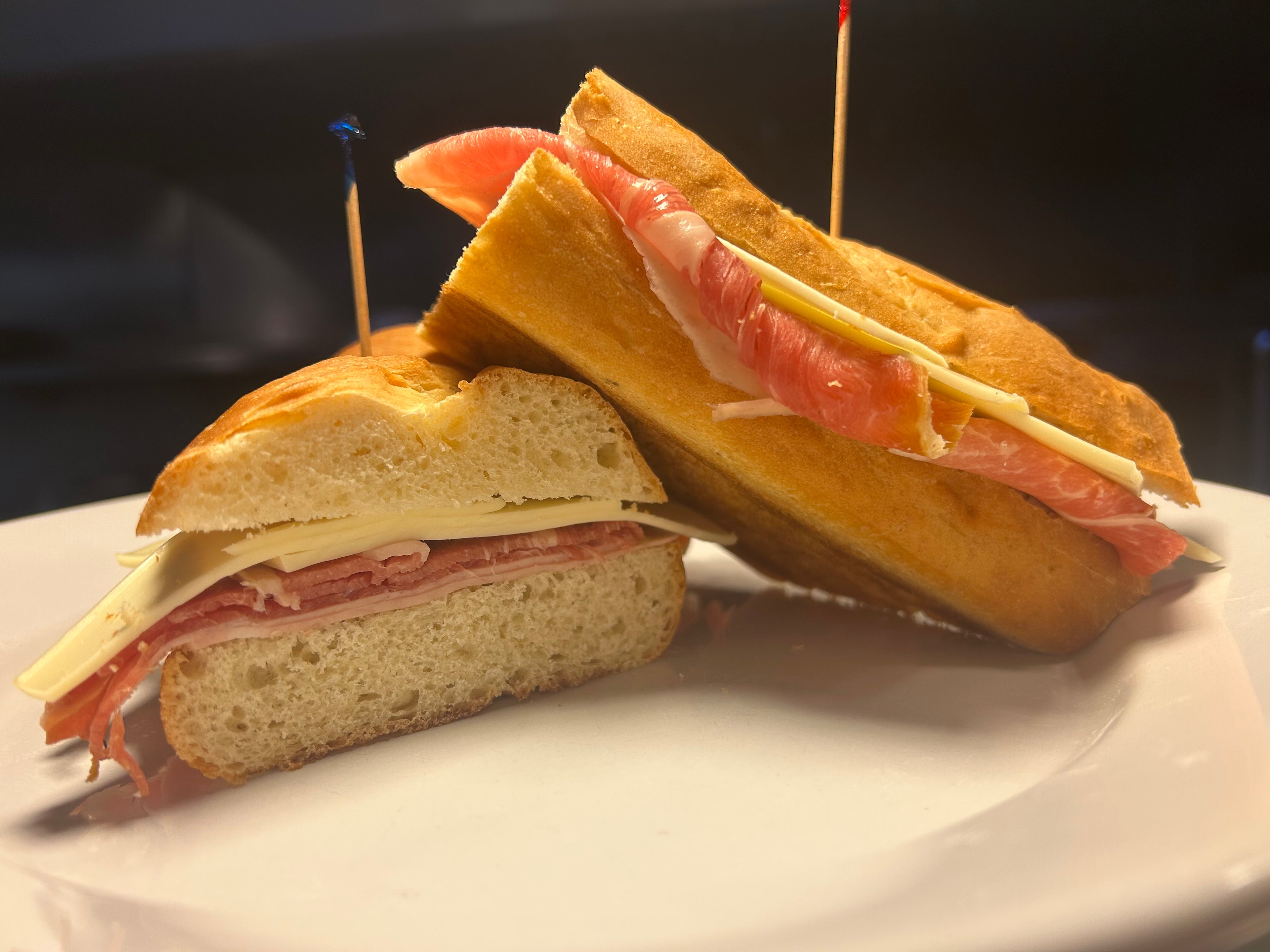 Half-cut sandwich with ham and cheese on a white plate against a dark background
