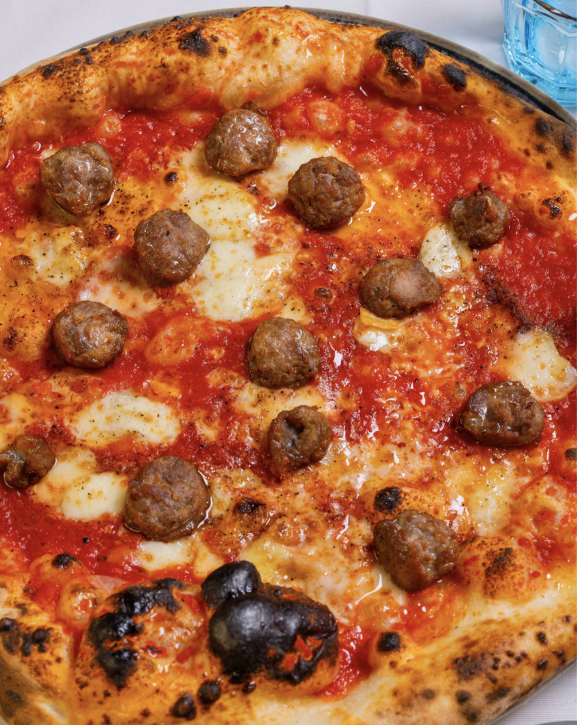 A close-up image of a thin crust pizza with tomato sauce, mozzarella, meatballs, and parsley.