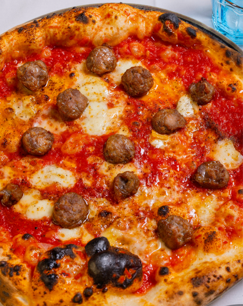 A close-up image of a thin crust pizza with tomato sauce, mozzarella, meatballs, and parsley.