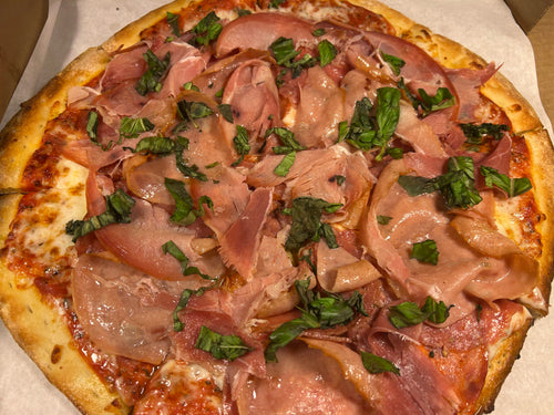 Close-up of a pizza with ham and spinach toppings on a white surface.