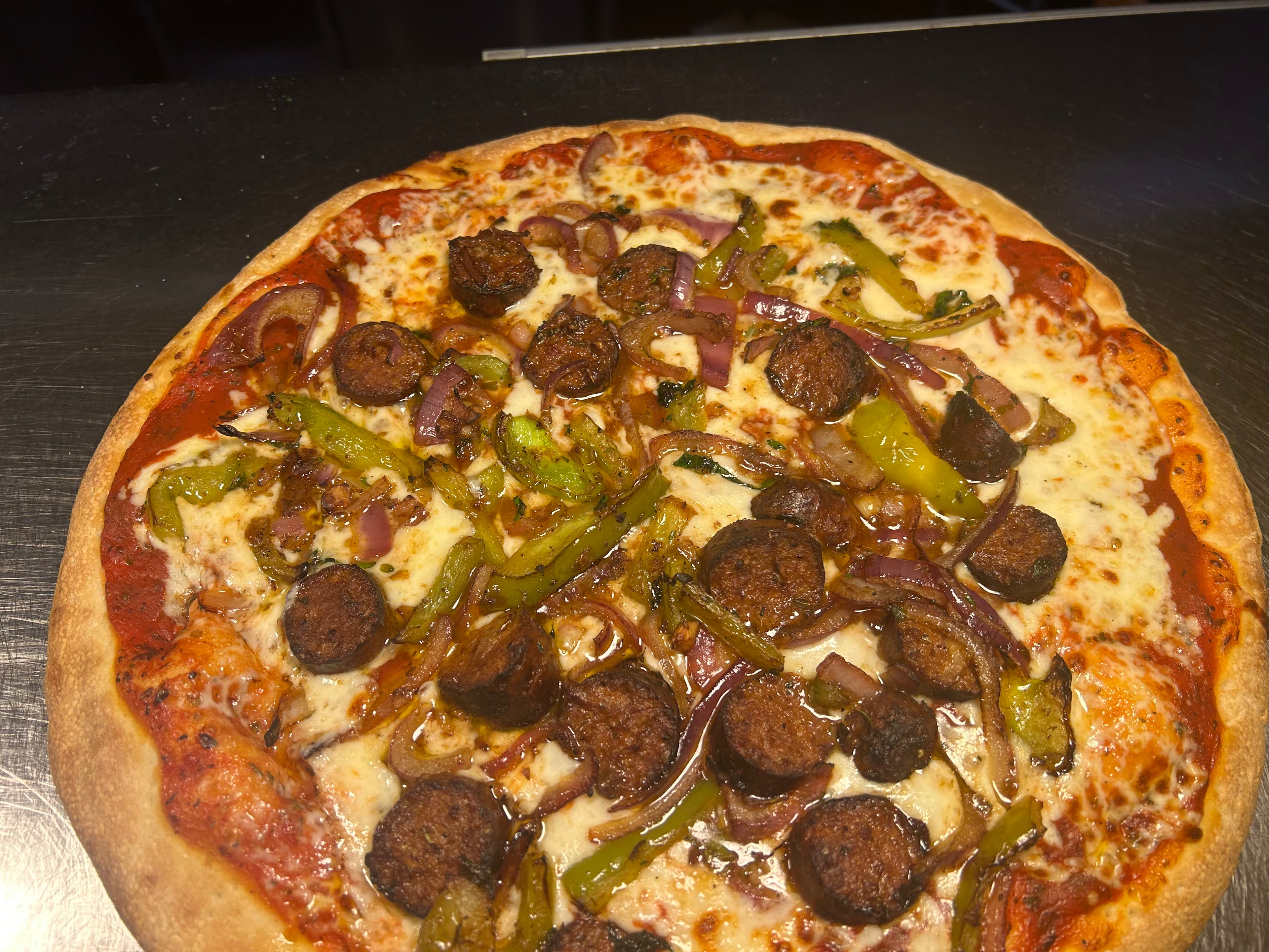 Pizza with sausages, peppers, and onions on a metal surface