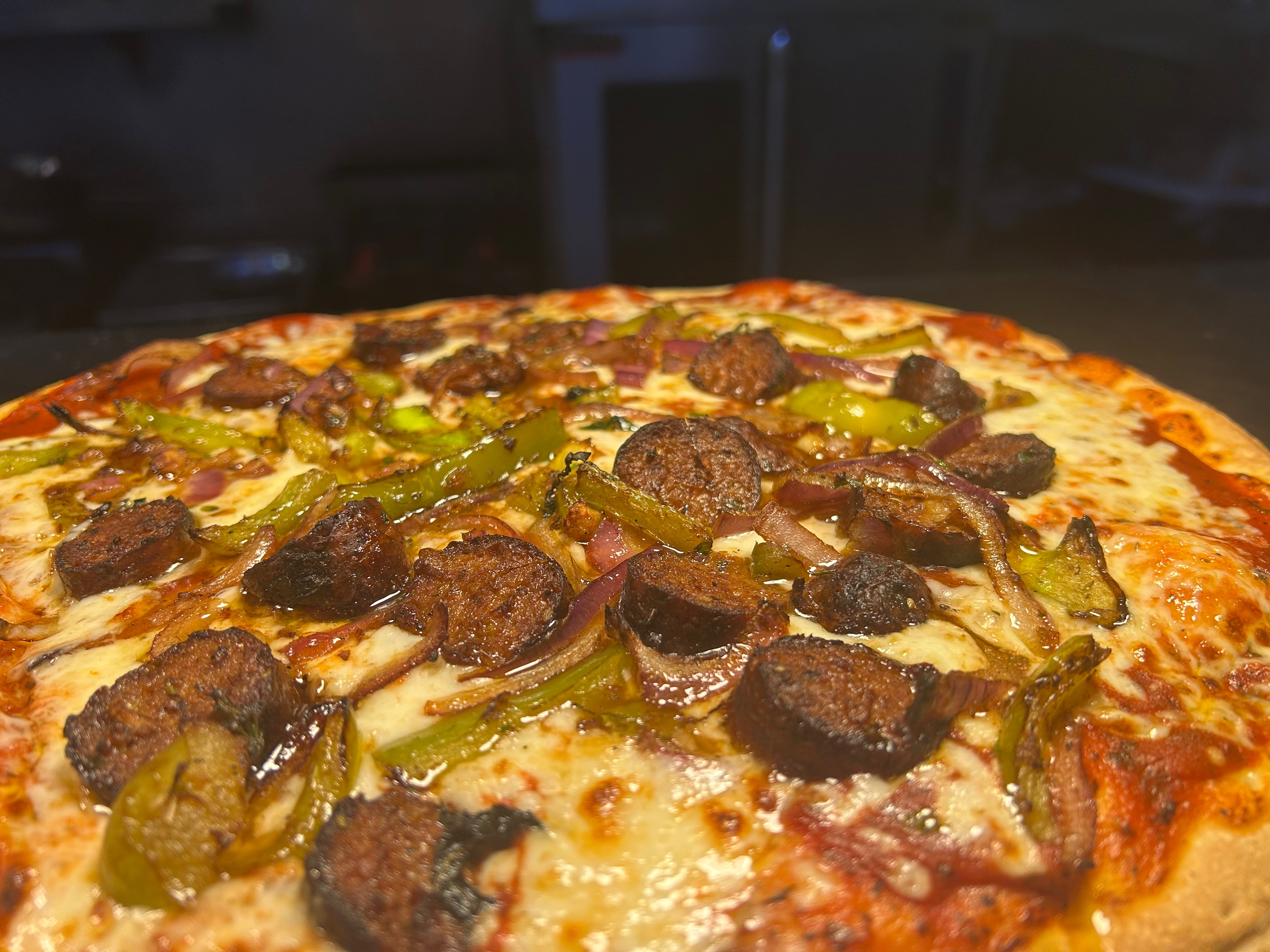 Pizza with sausage and green peppers on a wooden surface