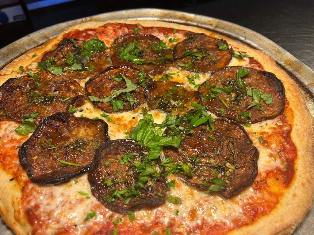 Pizza with eggplant slices and green herbs on a metal tray