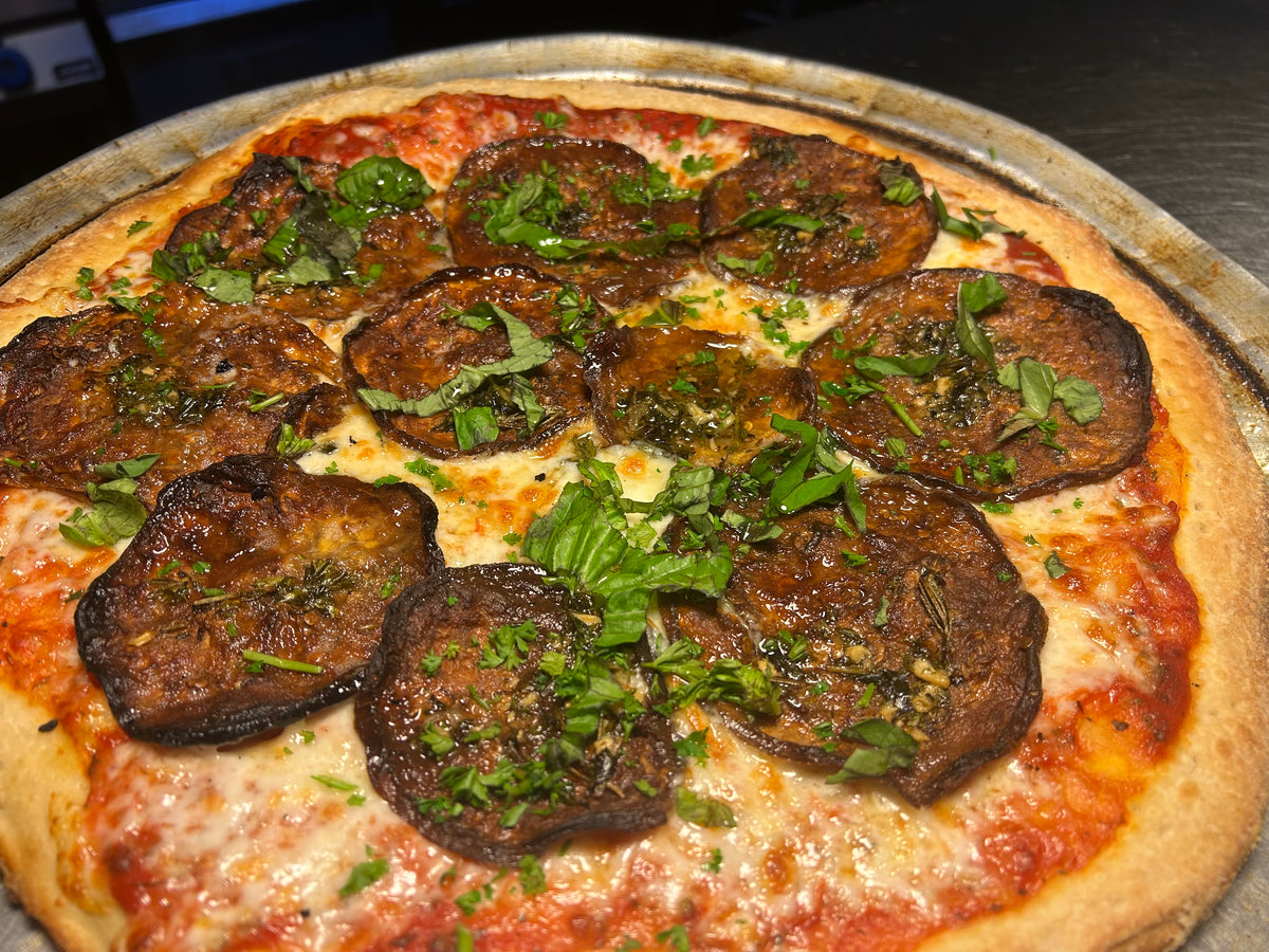 Pizza with eggplant slices and green herbs on a metal tray
